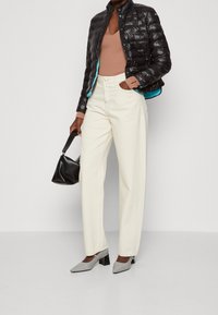 Czarna kurtka puchowa z turkusowym wykończeniem, beżowy sweter, kremowe spodnie o szerokich nogawkach oraz szare buty na słupku; trzyma czarną torebkę.