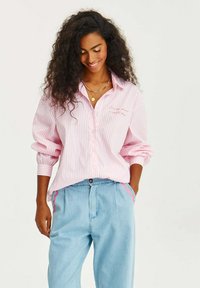 Ružovo-biely prúžkovaný košeľový top s vyhrnutými rukávmi, v kombinácii so svetlomodrými nohavicami s ružovými akcentami pozdĺž bočných švov.