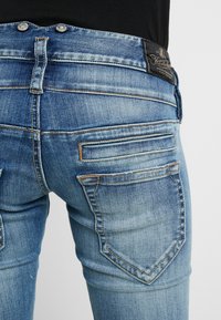Ljusblå denimjeans med en blekt tvätt. Har två bakfickor med horisontell sömnad och en märkesläderlapp i midjan.