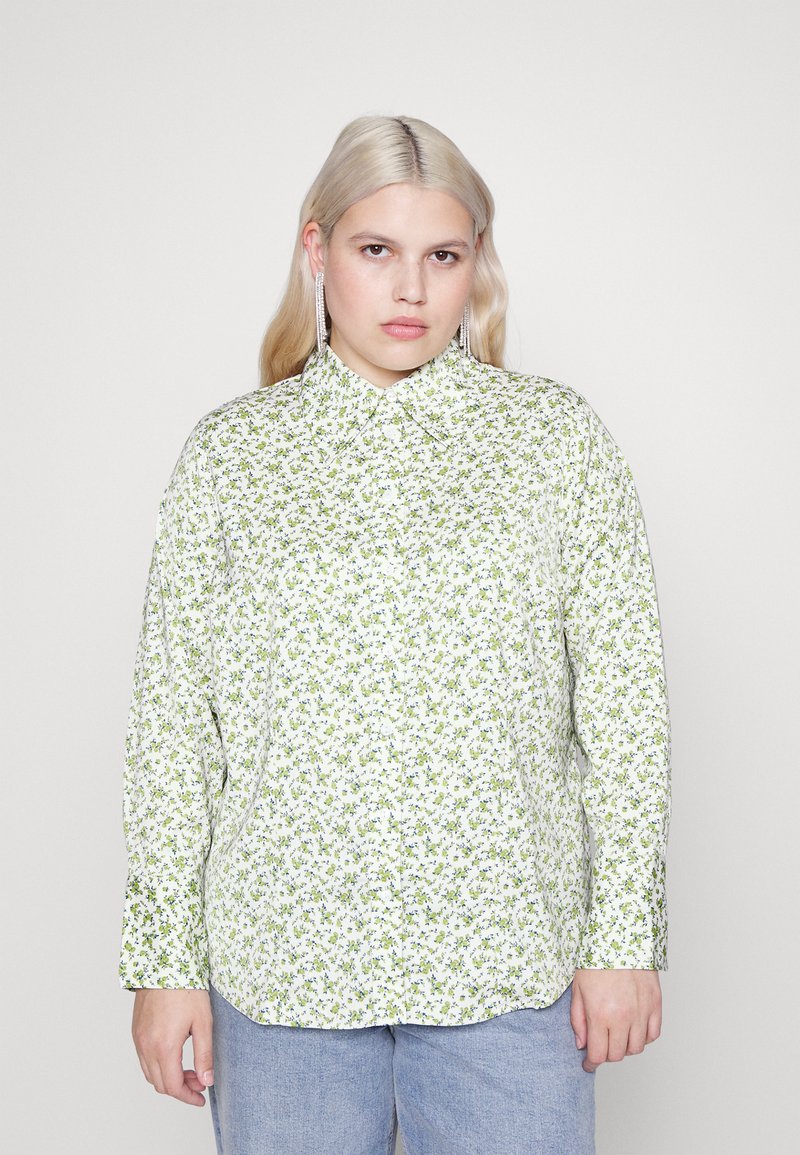 Camicia a maniche lunghe di colore bianco con un motivo floreale verde e blu. Presenta un colletto a punta e una vestibilità rilassata. Tessuto dalla superficie liscia.