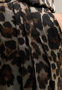 Tessuto con motivo leopardato, caratterizzato da macchie marroni e nere su uno sfondo grigio, con pieghe e una consistenza liscia e setosa.