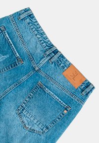 Jeans de mezclilla azul con una cintura alta, dos bolsillos traseros y una etiqueta de cuero marrón con marca en relieve. Textura suave y ligeros desgastes.