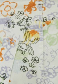 Tela blanca con un patrón colorido y alegre de flores y animales en naranja, morado, verde y negro, con costuras y líneas visibles.