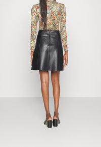 Svart läderskjorta med en slät yta, utställd design och dragkedjedetalj i ryggen. Bärs med en blommönstrad långärmad topp och klackade mules.