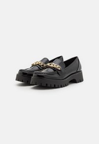 Black loafers with a shiny patent finish, featuring a gold-chain accent across the front and a chunky, ridged black platform sole.
