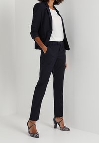 Marinblazer och byxor med en vit topp, kompletterad med mönstrade högklackade pumps. Skräddarsydd passform och släta tygtexturer.