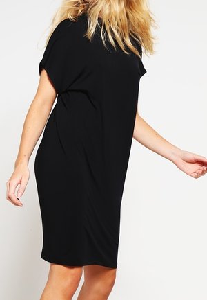 Robe noire à manches courtes en tissu doux, avec une coupe décontractée et un design à hauteur des genoux. Style minimaliste sans motifs ni accents visibles.