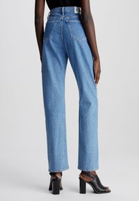 Vaqueros de mezclilla azul de talle alto con ajuste holgado, que cuentan con dos bolsillos traseros y una etiqueta negra con el logo en la cintura. Longitud hasta el tobillo.