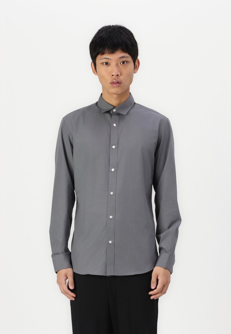 Camisa abotonada de manga larga en gris, con cuello punta, que presenta una textura de tela suave y botones blancos en el panel delantero.