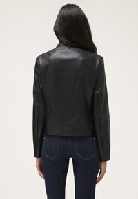 Giacca di pelle nera con un design aderente e una texture liscia, caratterizzata da maniche lunghe e un orlo corto. Abbinata a jeans in denim scuri.