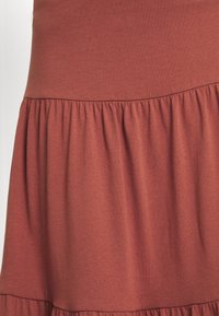 Robe en tissu doux de couleur rouille, avec un ourlet volanté et une taille froncée, d'une texture lisse et d'une longueur au-dessus du genou.