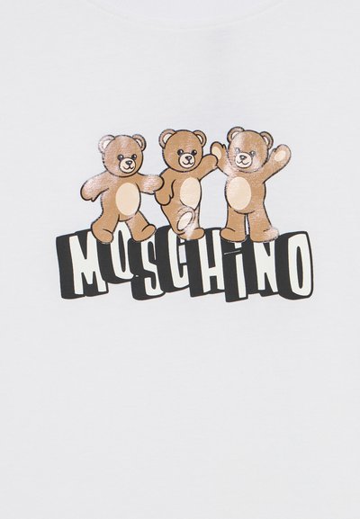 Τρεις καφέ αρκουδάκια με μπεζ κοιλίτσες στέκονται πάνω από τη λέξη "MOSCHINO" με έντονα μαύρα-λευκά γράμματα σε λευκό φόντο.