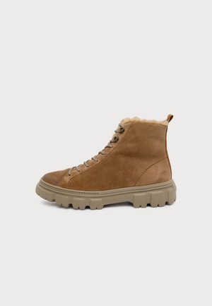 Botte montante en daim marron avec une épaisse semelle en caoutchouc beige et une doublure en fourrure, vue de profil sur un fond clair uni.