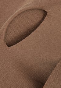 Närbild av brunt stickat tyg med en liten oval utskärning som avslöjar det inre texturerade stickade lagret.