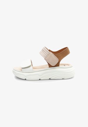 Sandales blanches et beiges avec une sangle élastique marron, semelle rembourrée, forme arrondie et semelle en caoutchouc texturée pour une meilleure adhérence.