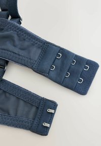 Tumši zils auduma krūštura pagarinājums ar trim rindu sudraba metāla āķiem un cilpām, klāts uz gaiši pelēka fona.