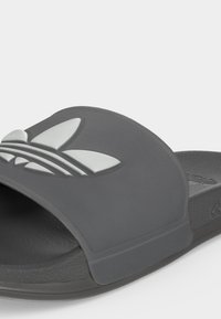 Κοντινό πλάνο ενός μαύρου Adidas σαγιονάρα με φαρδιά λουράκι που διαθέτει ανάγλυφο λευκό λογότυπο Adidas trefoil.