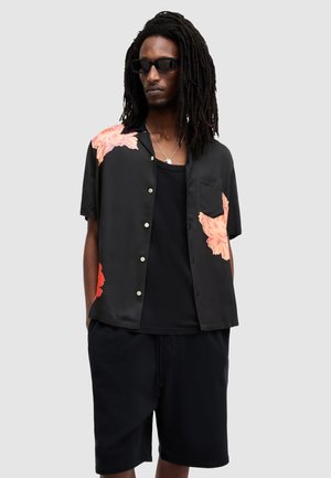 Kortærmet sort skjorte med stort lyserødt blomstermotiv, glat tekstur, knaplukning foran, båret over en sort tanktop og mørke shorts.