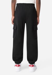 Čierne cargo nohavice vyrobené z mäkkého materiálu, s dvoma bočnými vreckami, elastickým pásom a manžetami na členkoch. V kombinácii s bielymi teniskami.