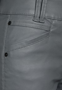 Gros plan sur un pantalon en cuir gris montrant la poche avant avec des rivets noirs et des passants de ceinture cousus.