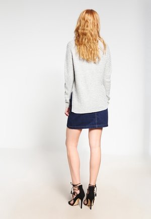 Maglione a maglia grigio chiaro con vestibilità ampia e spacchi laterali, abbinato a una gonna di jeans scura e sandali neri con tacco alto, visto da dietro.