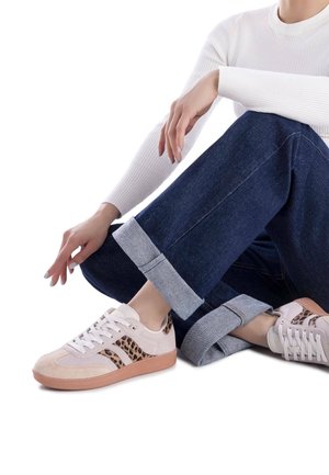 Baskets en daim beige clair avec des accents de motif léopard, lacets blancs et une semelle en caoutchouc texturée. Associées à un pantalon en denim foncé avec un ourlet roulé.