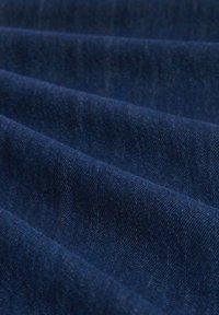 Mørkeblåt denimstof har en glat tekstur med subtile variationer, der viser foldede lag og en let glans.