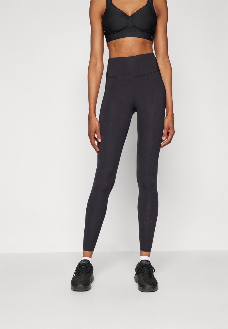 Black high-waisted leggings made of stretchy fabric featuring subtle dotted accents along the outer sides, paired with black athletic shoes.