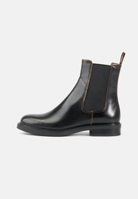 Botas Chelsea de cuero negro con paneles laterales elásticos, punta redondeada y acabado suave. Presenta un tacón corto y una lengüeta en la parte posterior.