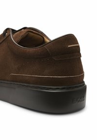 Chaussure décontractée en daim marron avec une semelle noire épaisse, des détails cousus et un logo "BOSS" embossé sur le talon.