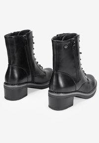 Botines de cuero negro hasta el tobillo con punta redonda, cremalleras en los lados, cordones en la parte delantera y un tacón grueso. Textura suave con un detalle de herrajes mínimo.