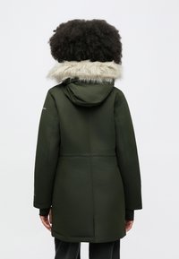 Lange olijfgroene parka met een kap gevoerd met bont, met een getailleerde pasvorm, ritssluitingen en elastische manchetten voor warmte.