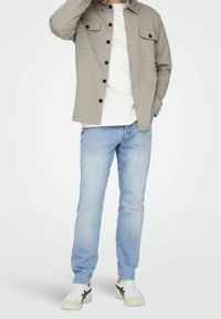 Gray button-up shirt with two chest pockets, white t-shirt underneath, light blue jeans, and white sneakers with black accents.