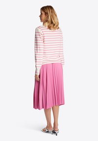 Camiseta de manga larga a rayas en blanco y rosa con puños acanalados, combinada con una falda plisada rosa hasta la rodilla. Sandalias de tacón plateadas visibles.