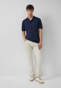 Marine gestreepte polo met kraag, korte mouwen en een borstzak, gecombineerd met lichtgekleurde broeken en twee-kleurige sneakers.