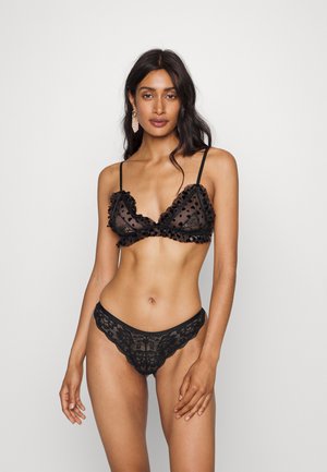 Mustmust mustrõngaste komplekt, mis sisaldab ruffle äärtega bralette'i ja läbi paistvat kangast, kokku sobitatud pitsist stringide paariga, milles on keerukad detailid.