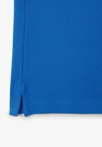 Tissu bleu texturé avec une couture latérale et une petite fente près de l'ourlet sur un fond clair.