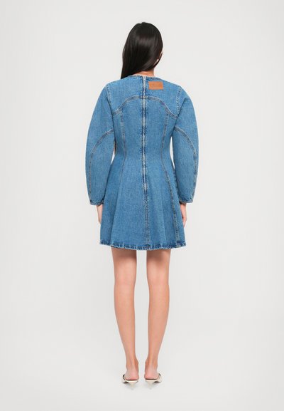 Džínová šaty s dlhými puff rukávmi, priliehavým živôtikom, rozšírenou sukňou a nerovným lemom. Ponúka štruktúrovanú modrú látku a hnedú nášivku na zadnej strane.