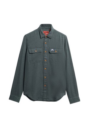 Dunkelgrünes langärmliges Hemd mit Knopfleiste, zwei geknöpften Brusttaschen, braunen Knöpfen und einem kleinen rechteckigen Logo-Patch auf der rechten Tasche.