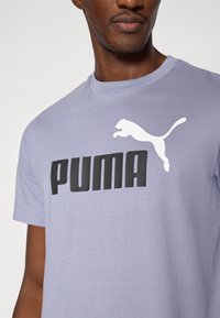 Μωβ βαμβακερό μπλουζάκι με μαύρο λογότυπο "PUMA" και άσπρη σιλουέτα που πηδάει, στρογγυλή λαιμόκοψη και κοντά μανίκια.