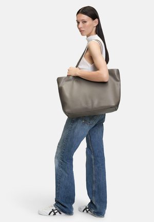Sac fourre-tout en cuir gris avec une texture lisse et un design minimaliste, arborant un logo discret et une bandoulière réglable.