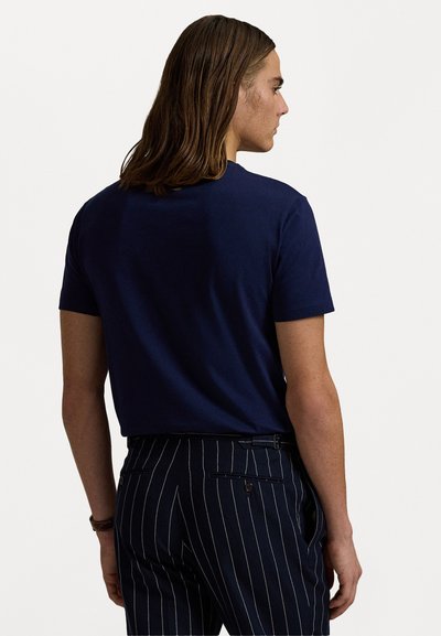 Sötétkék, rövid ujjú pamut póló hátulról nézve, sötét csíkozott nadrággal párosítva, sima textúrával és letisztult dizájnnal.