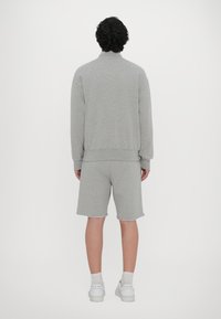 Hanorac gri din bumbac cu mâneci lungi și manșete ribbate, asociat cu pantaloni scurți gri asortați, având un tiv nefinisat, și adidași albi.
