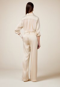 Beiger satin Jumpsuit mit Kragen, langen Ärmeln, elastischem Bund und weiter Beinform. Glatte Textur mit entspannter Passform.