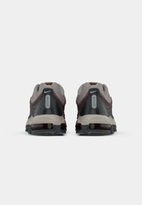 Pāris Nike Max Air sporta apavu pelēkā, melnā un oranžā krāsā, skatīti no aizmugures, izceļot gaisa amortizāciju zoles.