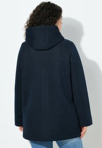 Tmavě modrá kapucí opatřená bunda z texturované pletené látky, s dlouhými rukávy a prodlouženým střihem, s volným střihem a bočními kapsami.