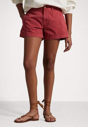 Rote Baumwollshorts mit lockerer Passform, klassischem Knopfverschluss und Seitentaschen. Kombiniert mit braunen Riemchensandalen.