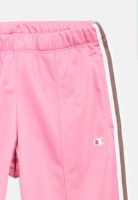 Ροζ αθλητικό σορτς με ελαστική μέση, πλαϊνές τσέπες, λευκές και καφέ πλαϊνές ρίγες, και μικρό λογότυπο Champion στο δεξί πόδι.