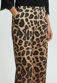 Pantalons à larges jambes en imprimé léopard beige et noir avec une texture lisse, dotés de poches latérales et d'une coupe ample pour un confort et une flexibilité accrus.