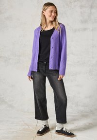 Violet neulecardigan, jossa on napit, käytetty mustan topin päällä. Yhdistetty mustiin leveälahkeisiin farkkuihin ja mustiin tennareihin, joissa on kreemiväriä.